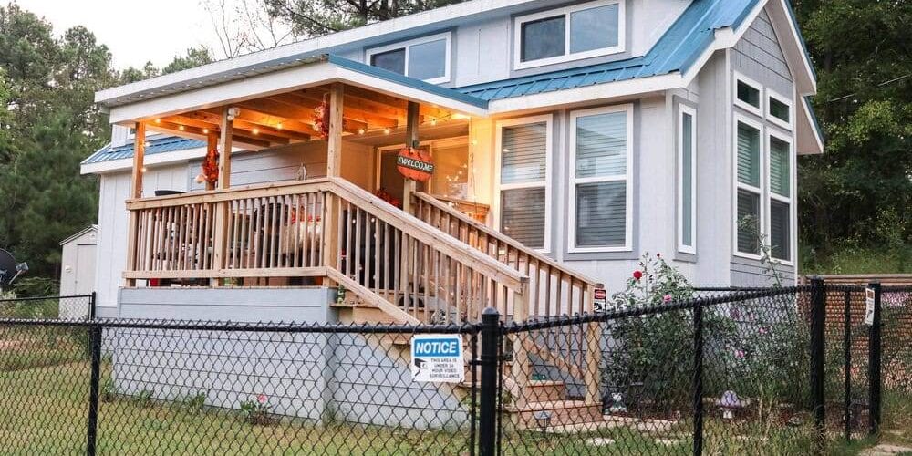 Blue,Tiny,House,With,Wooden,Porch,Surrounded,By,A,Black house surrounded by chain link fencing